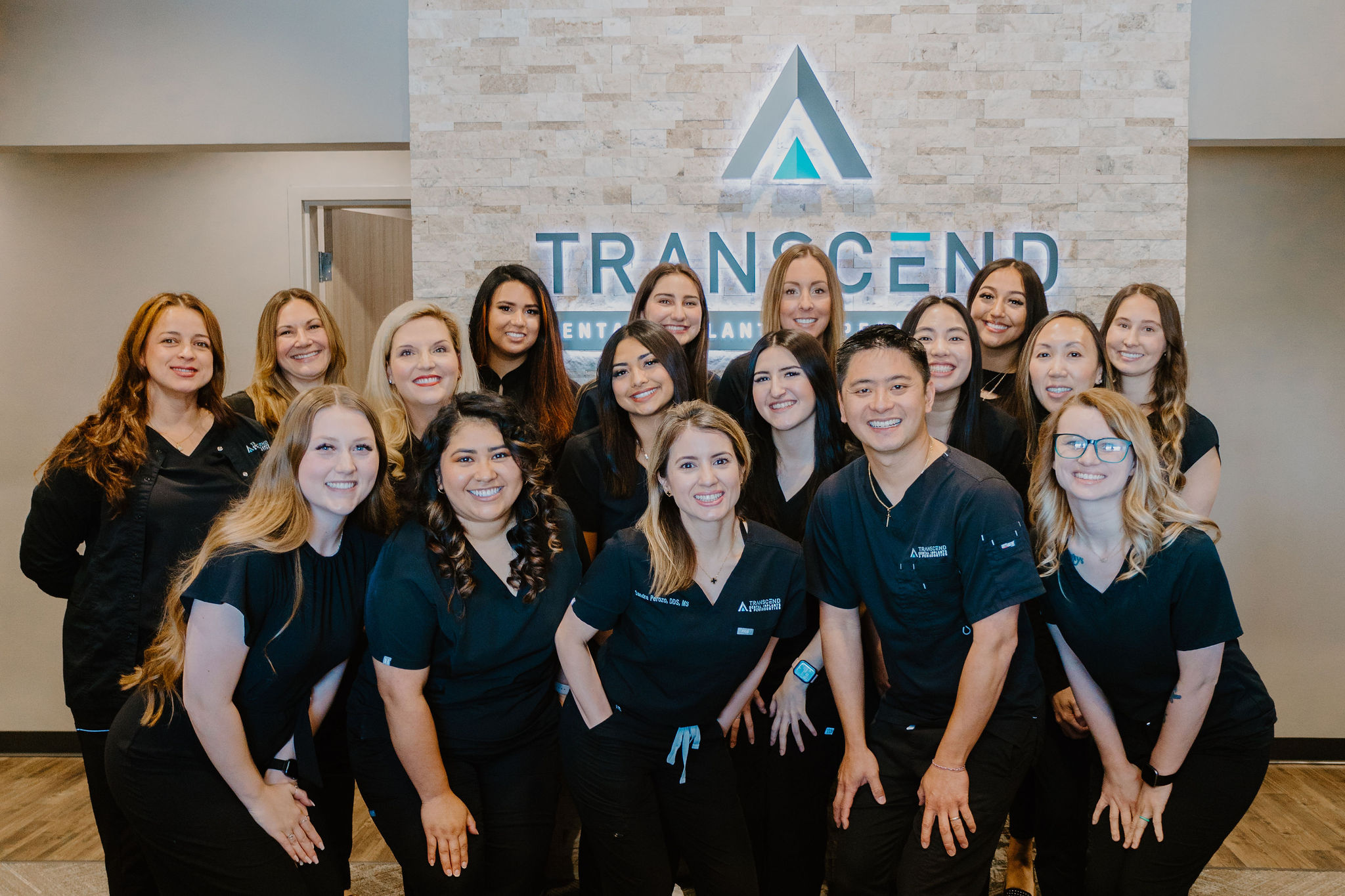 The full Transcend Dental Implants & Periodontics team in the lobby beneath the Transcend sign