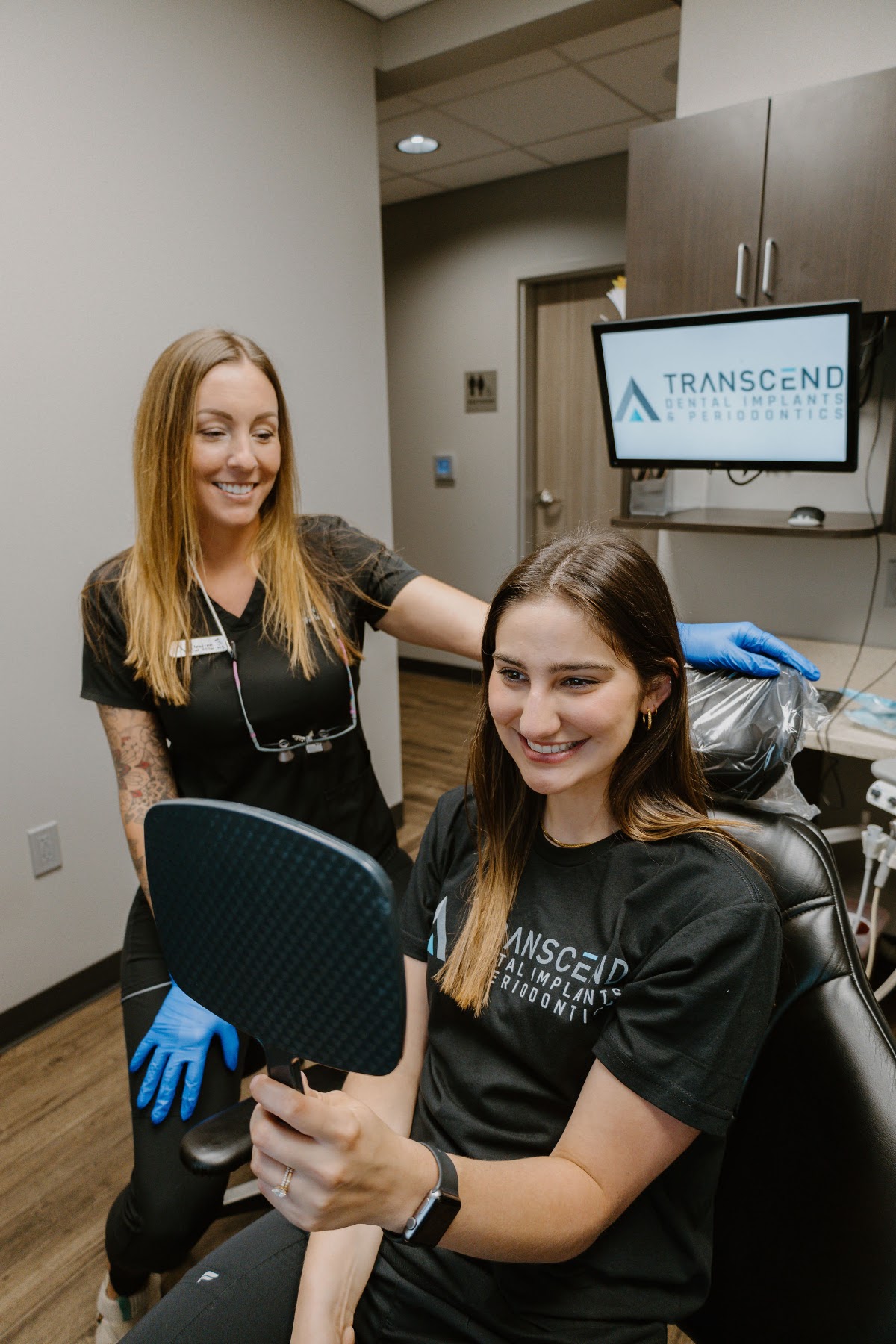 Patient smiling at her results in a hand mirror with a Transcend team member